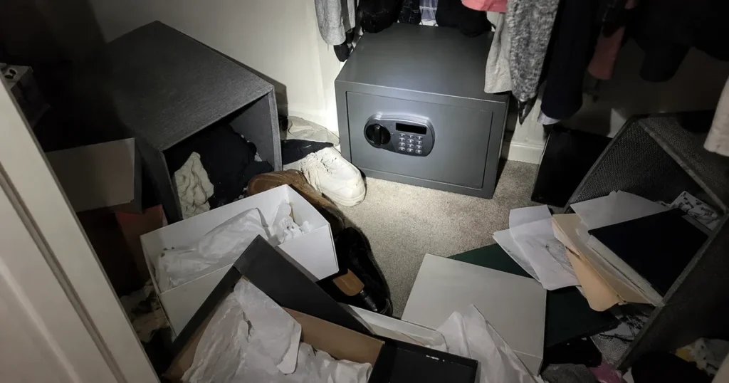 A gray home safe on a closet floor, surrounded by open boxes, shoes and scattered papers.
